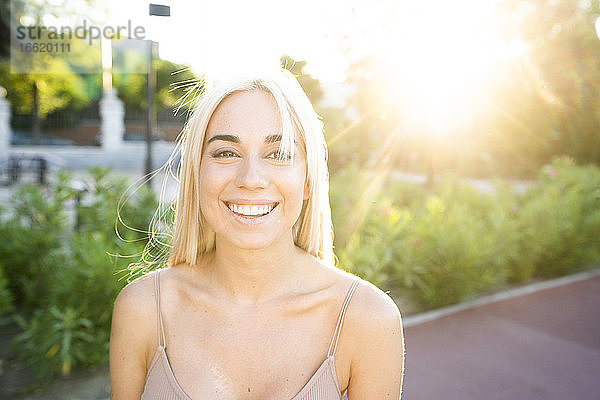 Nahaufnahme einer lächelnden jungen Frau mit blondem Haar im Park bei Sonnenuntergang