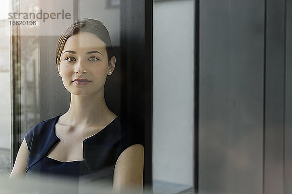 Nahaufnahme einer selbstbewussten Geschäftsfrau an der Wand eines Büros  gesehen durch eine Glastür