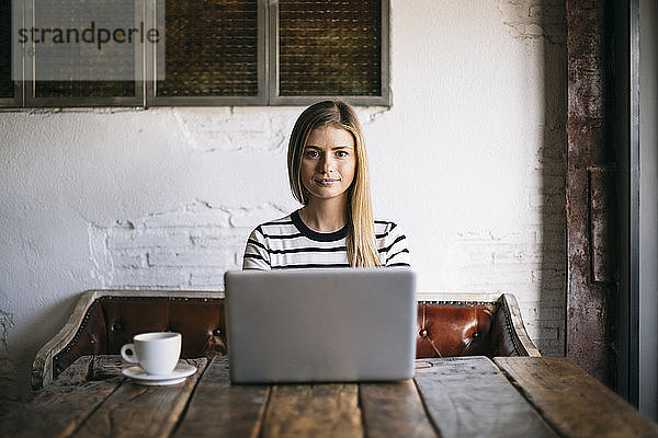 Frau  die in einem Café sitzt und einen Laptop benutzt