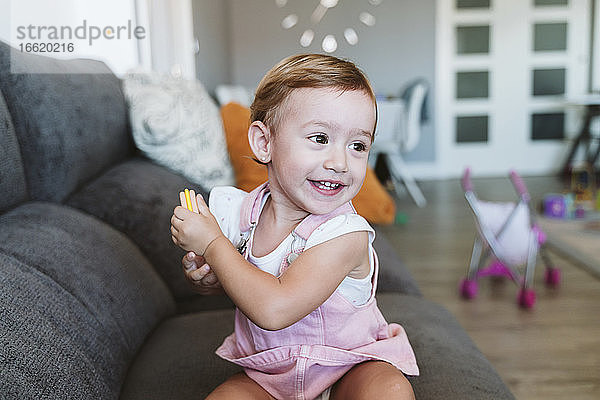 Ein kleines Mädchen hält einen Keks  während es auf dem Sofa zu Hause sitzt