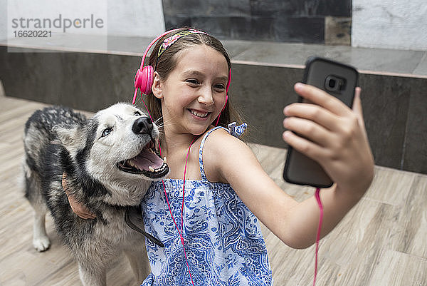 Lächelndes Mädchen  das ein Selfie mit einem Hund macht  während es zu Hause auf dem Boden sitzt