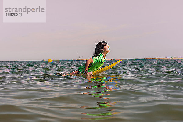 Unbekümmertes Mädchen Bodyboarding auf Meer gegen klaren Himmel bei Sonnenuntergang