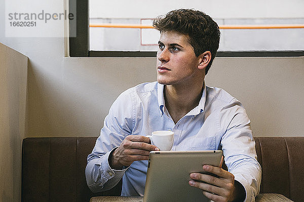 Gut aussehender junger Mann mit Kaffeetasse und digitalem Tablet  der in einem Café sitzt