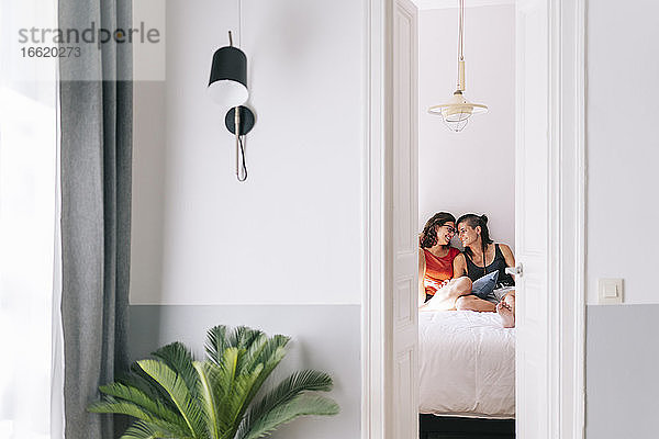 Lächelnde Freundinnen sitzen auf dem Bett im Schlafzimmer