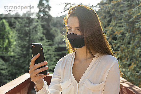 Junge Frau trägt Schutzmaske  während sie ein Selfie mit ihrem Smartphone macht
