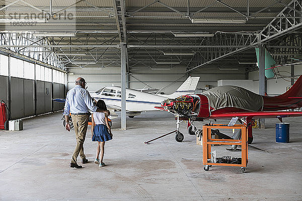 Enkelin und Großvater gehen in einem Flugzeughangar spazieren