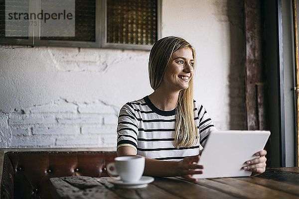 Lächelnde Frau  die in einem Café ein digitales Tablet benutzt und dabei wegschaut