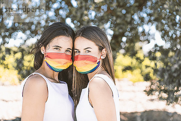 Junge Frauen mit mehrfarbiger Gesichtsmaske stehen vor einem Baum