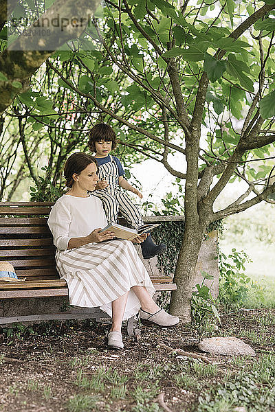 Schöne Frau und Junge beim Lesen eines Buches auf einer Bank im Hinterhof sitzend