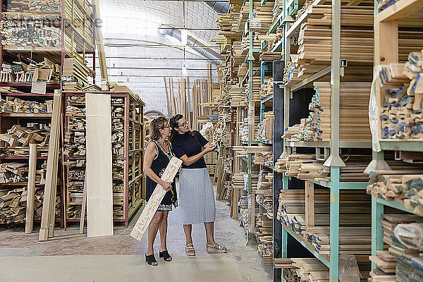 Frauen wählen eine verzierte Holzplatte aus  während sie in einem Lagerhaus in einer Fabrik stehen
