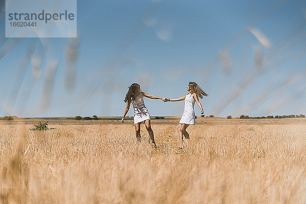 Lesbisches Paar hält sich an den Händen und spielt auf einem landwirtschaftlichen Feld