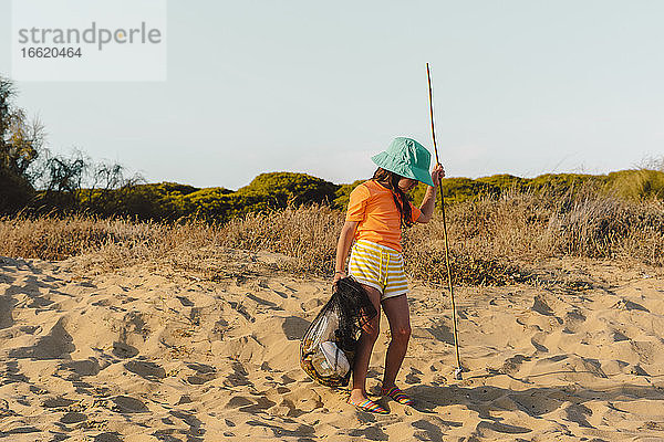 Mädchen  das Müll trägt  während es auf einem Ständer am Strand steht