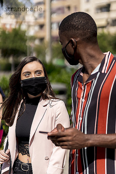 Junges Paar mit Gesichtsmasken bei einem Spaziergang in der Stadt während des Ausbruchs von COVID-19