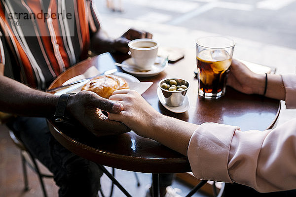 Romantisches junges Paar hält sich an den Händen  während es in einem Café etwas trinkt
