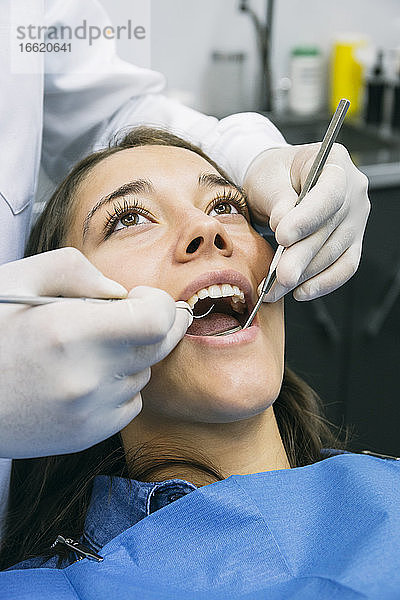 Zahnarzt mit Handschuhen bei der Untersuchung der Mundhöhle eines hübschen Patienten in einer Klinik