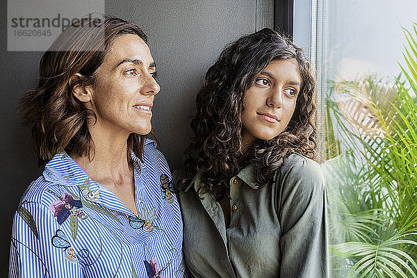 Mutter und Tochter schauen durch das Fenster  während sie zu Hause stehen