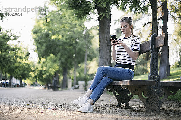 Frau schreibt Textnachrichten auf ihrem Smartphone  während sie in einem öffentlichen Park sitzt