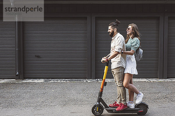 Lächelndes Paar fährt mit einem elektrischen Roller auf der Straße in der Stadt