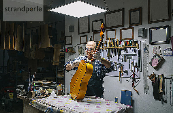 Mann hält Gitarre auf Werkbank bei der Arbeit in der Werkstatt