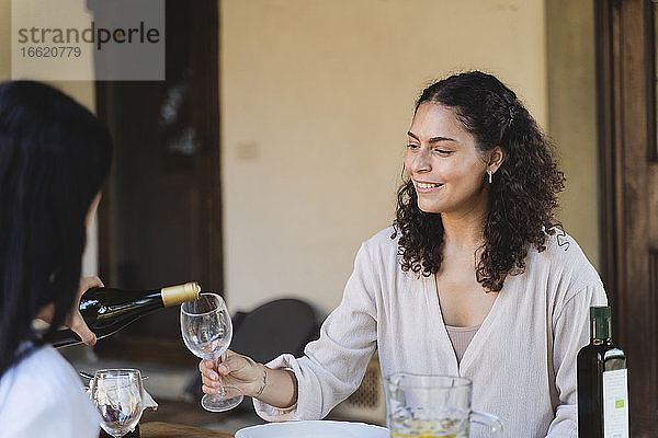 Frau gießt Champagner in das Weinglas eines Freundes  während sie an einem Tisch im Hinterhof sitzt