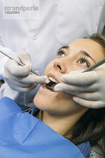Zahnarzt mit Handschuhen bei der Untersuchung der Mundhöhle einer Patientin in einer Klinik