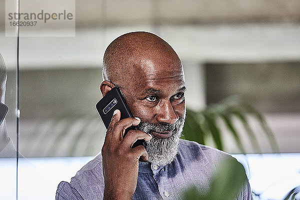 Lächelnder  selbstbewusster Geschäftsmann  der einen Anruf über sein Smartphone entgegennimmt