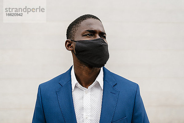 Männlicher Berufstätiger mit Gesichtsschutzmaske an der Wand während der COVID-19-Pandemie