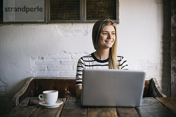 Lächelnde Frau  die wegschaut  während sie einen Laptop in einem Café benutzt