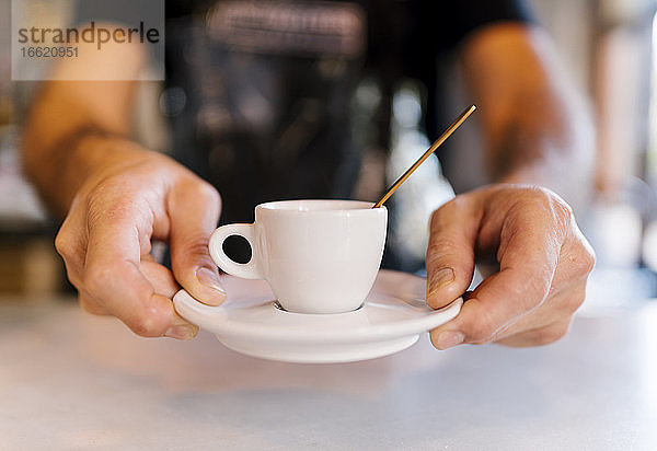 Männlicher Barista serviert Kaffee am Tresen eines Cafés