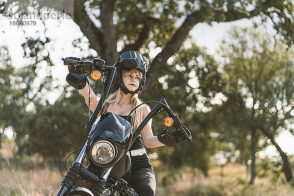 Schöne Frau mit Sturzhelm  die auf einem Motorrad gegen einen Baum sitzt