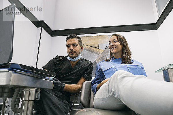 Attraktiv lächelnde Patientin  die mit den Erklärungen des männlichen Zahnarztes zur künftigen Behandlung in der Klinik zufrieden ist