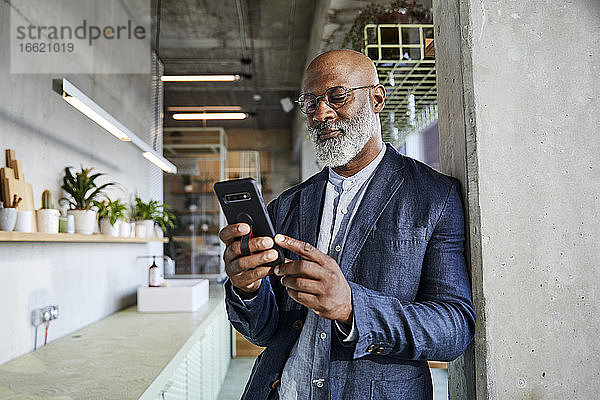 Älterer Mann  der zu Hause stehend eine Textnachricht auf seinem Smartphone schreibt