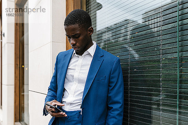 Junger männlicher Unternehmer  der sein Smartphone benutzt  während er sich in der Stadt ans Fenster lehnt