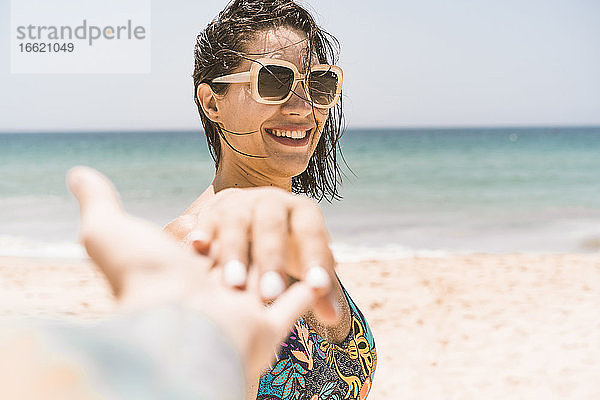 Lächelnde Frau mit Sonnenbrille hält die Hand eines Freundes am Strand von Valdevaqueros  Tarifa  Spanien
