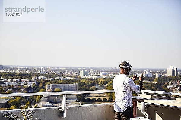 Älterer Mann  der ein Foto macht  während er sein Smartphone benutzt und auf der Terrasse eines Gebäudes steht