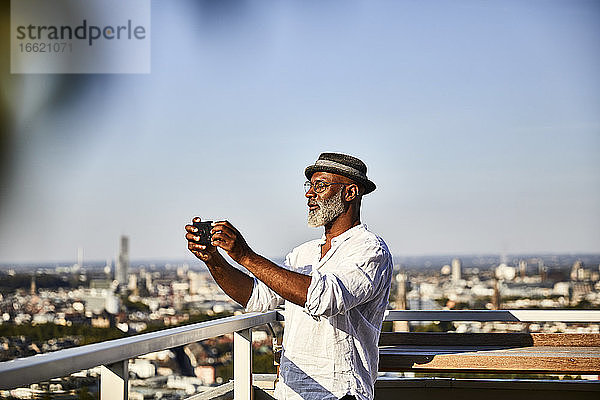 Älterer Mann  der ein Selfie macht  während er ein Smartphone benutzt  das auf einer Gebäudeterrasse steht