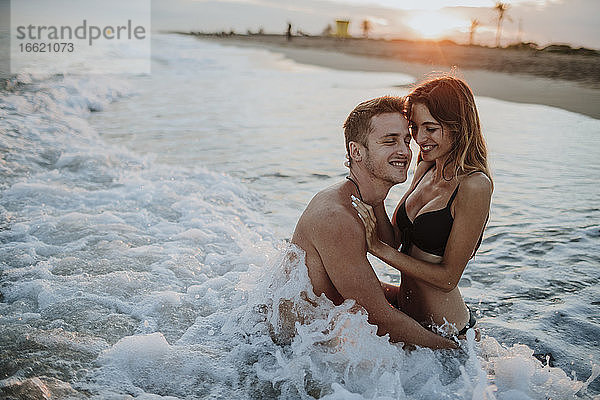 Lächelndes Paar genießt das Sitzen im Wasser am Strand