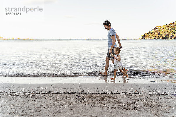 Glücklicher Vater  der mit seiner Tochter am Strand spazieren geht