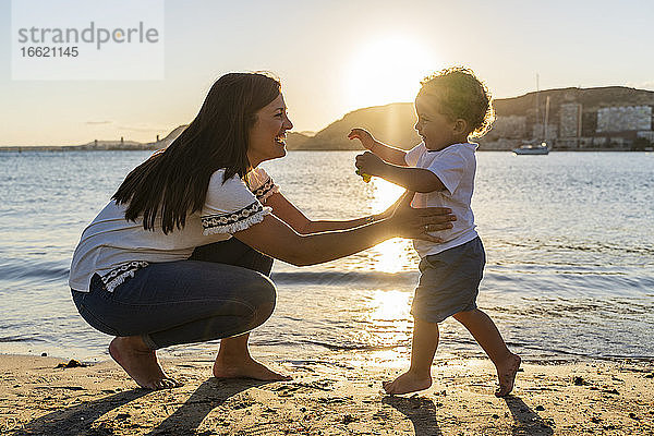 Fröhliche Mutter spielt mit ihrem Sohn am Strand bei Sonnenuntergang