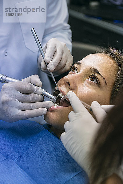 Zahnarzt bei der zahnärztlichen Behandlung einer hübschen Patientin mit Hilfe eines Assistenten in der Klinik