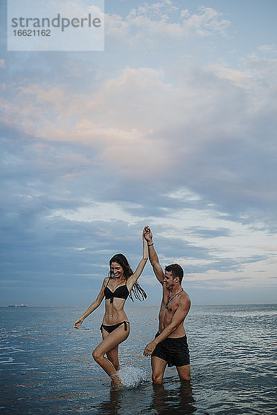 Paar in Badekleidung  das im Wasser am Strand spazieren geht