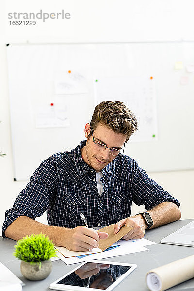 Architekt schreibt auf Papier  während er am Schreibtisch im Büro sitzt