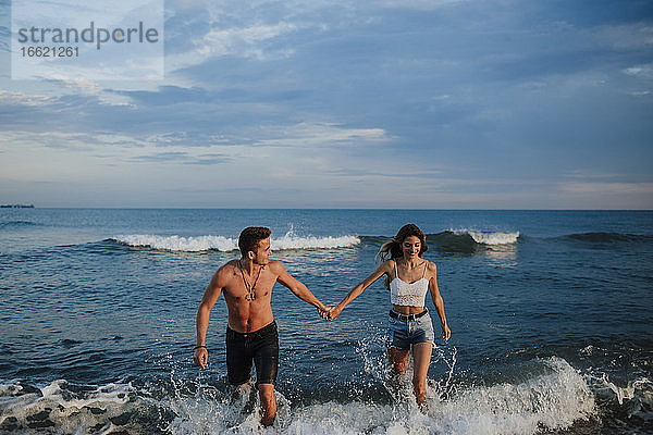 Paar hält sich an der Hand  während es im Wasser am Strand spazieren geht