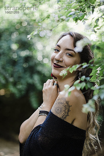 Junge Frau lächelnd bei einer Pflanze im Park stehend