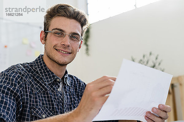 Lächelnder Mann hält Papier bei der Arbeit im Büro