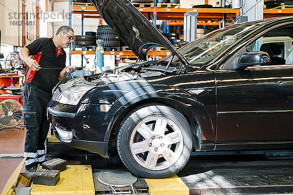 Männlicher Mechaniker  der ein Auto repariert  während er in einer Autowerkstatt steht
