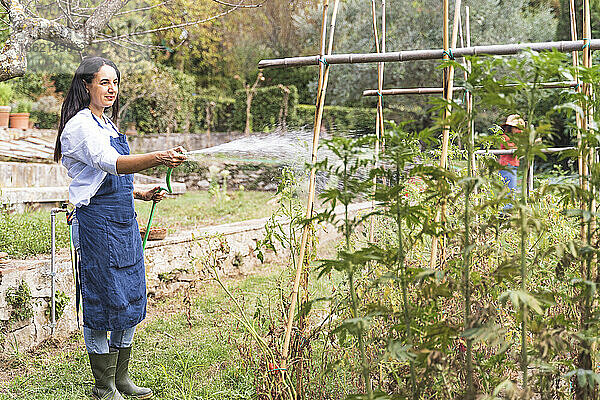Frau bei der Gartenarbeit  während sie im Gemüsegarten Wasser aus dem Schlauch sprüht