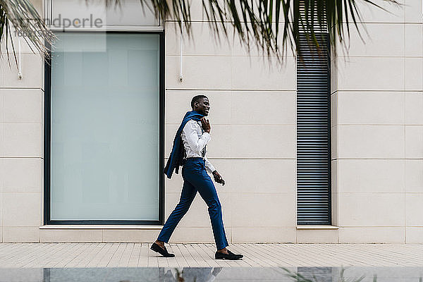 Lächelnder männlicher afrikanischer Berufstätiger  der auf dem Bürgersteig in der Stadt geht