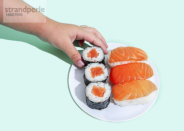 Hand eines kleinen Mädchens  das ein Stück Maki-Sushi aufhebt