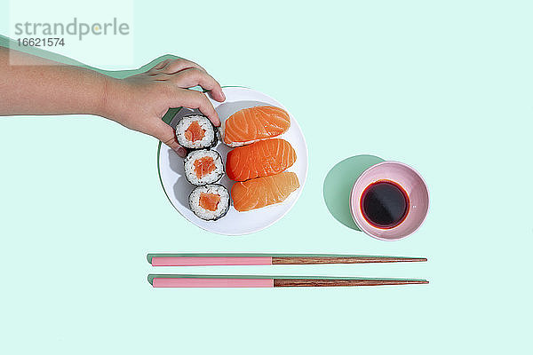 Hand eines kleinen Mädchens  das ein Stück Maki-Sushi aufhebt